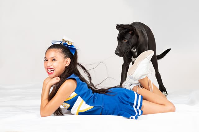 Girl in cheerleading constumeposing on floor with black lab puppy