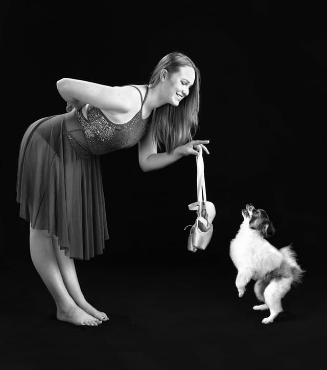 Girl dangling toe shoes in front of small dog on hind legs